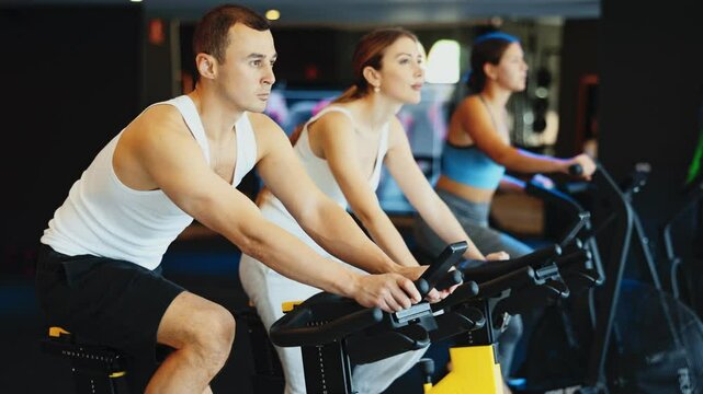 Sportive young man doing spin bike exercises in well-equipped gym during training session