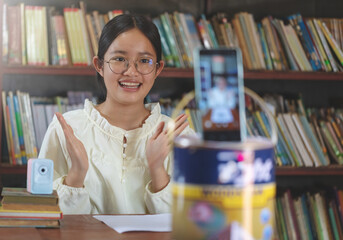 A girl is teaching online with her smartphone against a bookshelf background.To share video on tiktok social media application