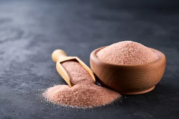 pink himalayan salt in a wooden bowl on a black stone table, selective focus. © Igor Dudchak