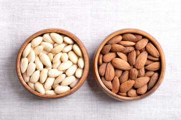 Almonds with skin and skinless almonds in wooden bowls on linen. Fruits of Prunus amygdalus, syn. Prunus dulcis, with seed coats and blanched, ready-to-eat as snack or as ingredient for baking. Photo