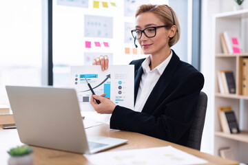 Businesswoman in thirties presenting financial graphs during online meeting using laptop, showcasing growth data.