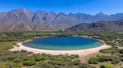 Obraz premium Aerial view of a round lake with turquoise water, sandy shores, and green bushes against a mountain backdrop