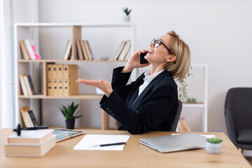 Middle-aged Caucasian woman in business attire talking on phone in modern office workspace