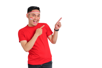 Cheerful young Asian man celebrating Indonesian independence day pointing aside at copy space isolated on transparent background