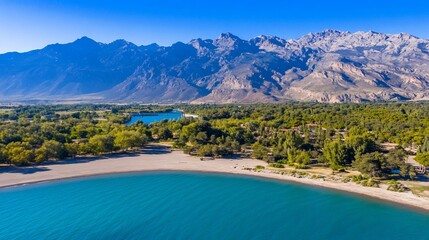 Fototapeta premium Aerial view of a serene lake with a sandy shore, surrounded by green trees & mountains