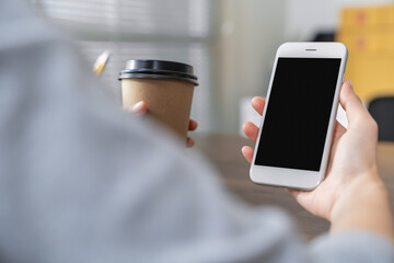 Hand holding smartphone with a blank screen on table, for putting advertising to promote.
