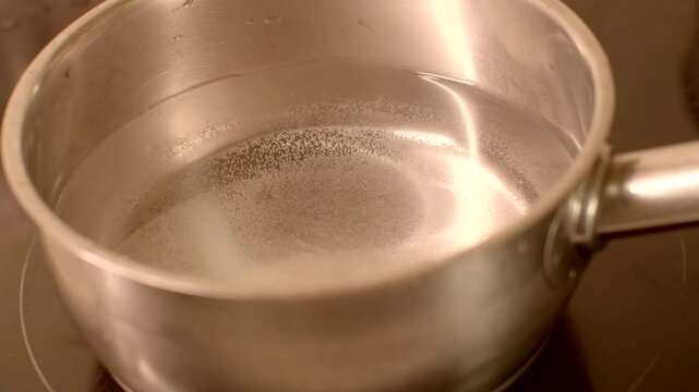 A metal pot filled with water is currently heating up on a stove burner, preparing for cooking