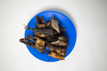 A blue plate filled with pieces of deep-fried fish, crispy and dark golden brown, served on a white...