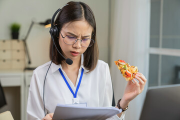 Asian businesswoman eating pizza while working with clients due to rush hour.