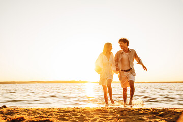 Smiling beautiful woman and her handsome boyfriend. Excited couple in casual clothes. Happy cheerful family. Female and man run at sunrise over sea beach outdoors. Run at seaside in summer day