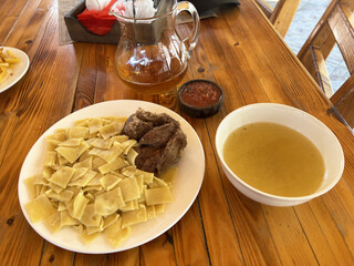 Traditional dagestani meal with beef, homemade pasta, broth, and tea on rustic wooden table