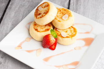 Delicious sweet cottage cheese pancakes served with fresh strawberries and cream on a white plate for breakfast