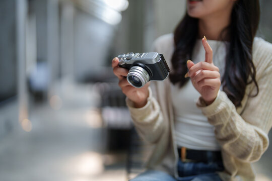 Photographer is showing how to use professional compact mirrorless camera explaining something with her finger while holding a camera in her hands