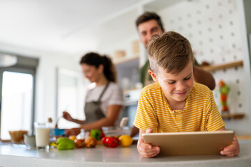 Happy young family with kid in kitchen have fun using modern tablet together, enjoying weekend