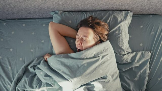 A person peacefully sleeps under a soft blanket in a cozy bedroom. Natural light filters in, creating a serene and calming atmosphere. Morning thoughts linger as the day begins.