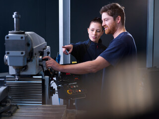 Engineer pointing at CNC machine near colleague in factory
