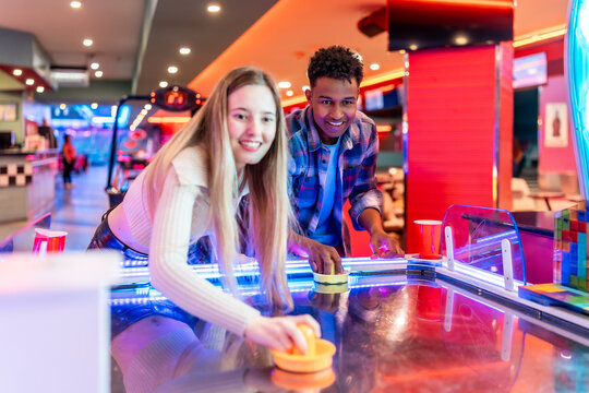 Young multiethnic friends playing air hockey in entertainment center