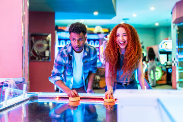 Friends playing air hockey in amusement arcade
