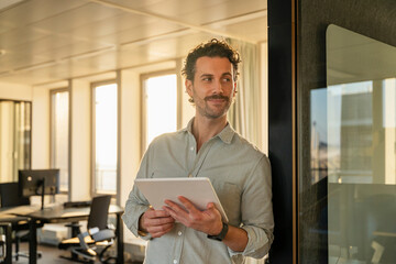 Man in office holding a tablet and smiling during sunset