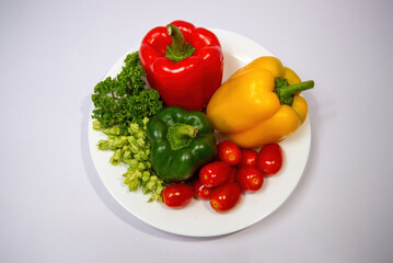 Colorful bell peppers, cherry tomatoes, and parsley on a white plate. Fresh healthy ingredients.