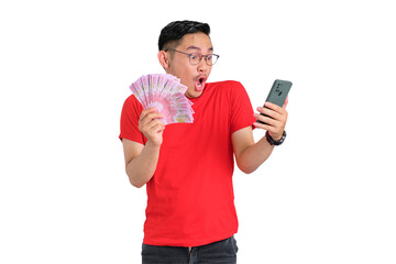 Shocked young Asian man using mobile phone and holding money banknotes isolated on transparent background