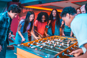 Excited multiethnic friends playing foosball in entertainment venue