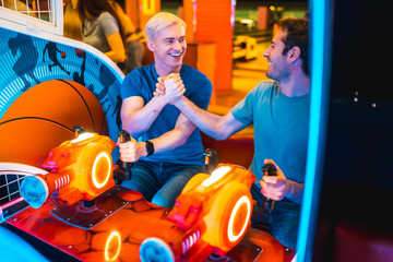 Two friends shaking hands while playing arcade game at amusement park