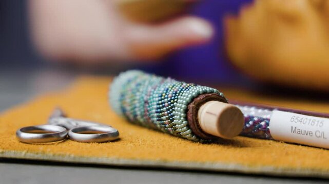 Macro shot of vibrant beads in sharp focus while a M&eacute;tis elder works on traditional beadwork in the blurred background. A peaceful moment highlighting Indigenous artistry and craftsmanship shot in 4k.