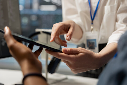 Data center engineering team analyzing software logs metrics on tablet, optimizing storage systems. Close up of server farm coworkers inspecting resource utilization on device