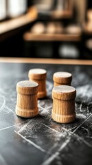 Four small, light brown wooden cylinders stand on a dark, dusty surface.  Flour dusted