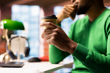 Relaxed man drinking coffee at home while watching TV show on laptop. Person starting day with hot beverage, enjoying leisure time in apartment, consuming entertainment media content