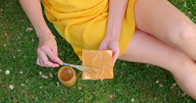Woman in yellow dress spreading peanut butter on toast in a sunny park.