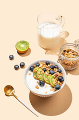 Natural yogurt with granola, kiwi and blueberries in a bowl on a beige background.
