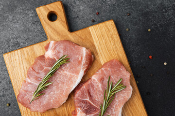 Fresh pork chops garnished with rosemary on a wooden cutting board