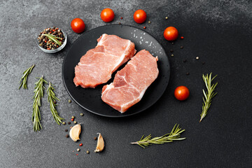 Freshly prepared pork chops with herbs and tomatoes laid on a dark surface