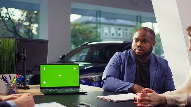 Salesman using isolated screen laptop to present car addons options to clients, trying to sway them to make purchase. Showroom agent offers warranty to customers, holding chroma key notebook, camera B