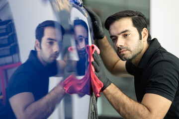 Professional car detailer wearing black gloves and a black polo shirt polishes a blue vehicle using...