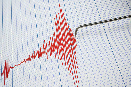 A close-up of a seismograph recording an earthquake. The needle draws red lines on the paper, indicating strong tremors.