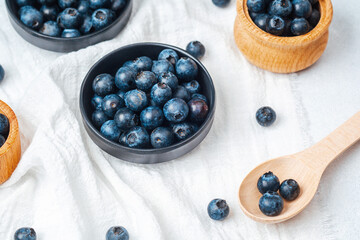Fresh blueberries in bowls and scattered on a white cloth surface