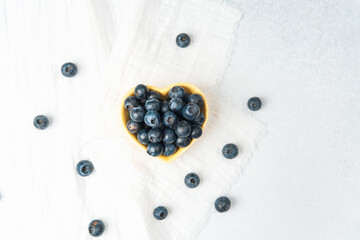 Fresh blueberries arranged neatly in a heart-shaped bowl on a white tablecloth