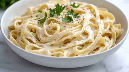 Rich creamy fettuccine Alfredo with parsley in white bowl on marble