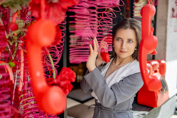 a woman in a gray suit standing outside a cafe decorated with hanging telephones. She's holding one...