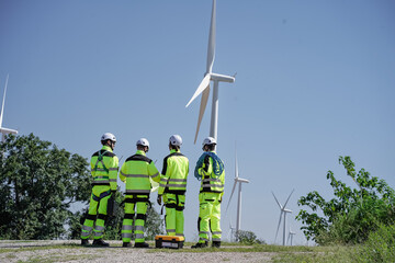 Maintenance engineer team standing at windmills at wind turbine farm. Group of people wear safety...