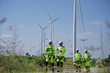 Maintenance engineer team standing at windmills at wind turbine farm. Group of people wear safety...