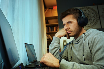 Unfocused man sitting at desk with hand on face, looking at screen. Freelancer distracted at home...