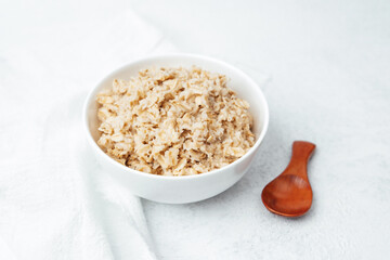 Healthy cooked oatmeal with a wooden spoon on a light background