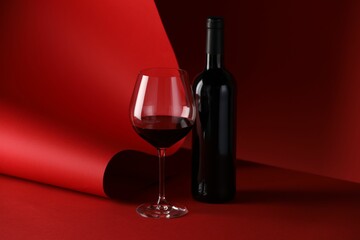 Bottle and glass of tasty wine on red background