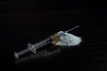The image shows a syringe with a needle lying on a pile of white powder, similar to heroin, on a...