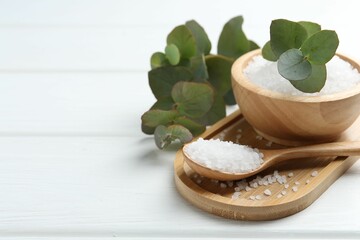 Sea salt and beautiful eucalyptus branches on white wooden table, closeup. Space for text