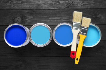 Cans with paint in shades of blue and brushes on black wooden background, top view